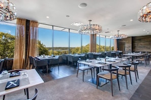 A modern restaurant with high ceilings, large windows, and elegant chandeliers.