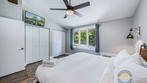 A bedroom with a bed, a ceiling fan, a window with curtains, a wall-mounted TV, and a wardrobe. - Modern Lake Geneva Condo With Pool and Patio (Lake Geneva)