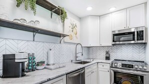 A modern kitchen with white cabinets, a stainless steel microwave, a built-in oven, a coffee maker, and a herringbone-patterned backsplash. - Modern Lake Geneva Condo With Pool and Patio (Lake Geneva)