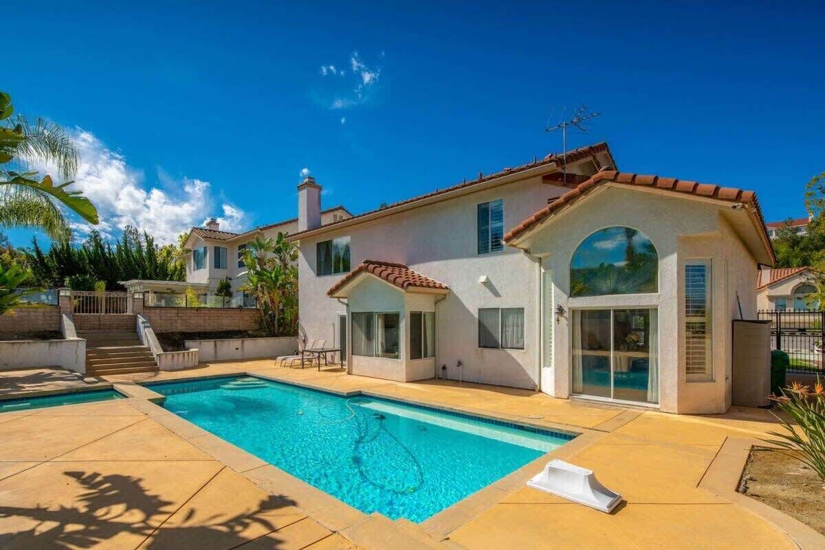 Een tweelaags huis met een zwembad, een overdekt terras en een groot raam met uitzicht op het zwembad.