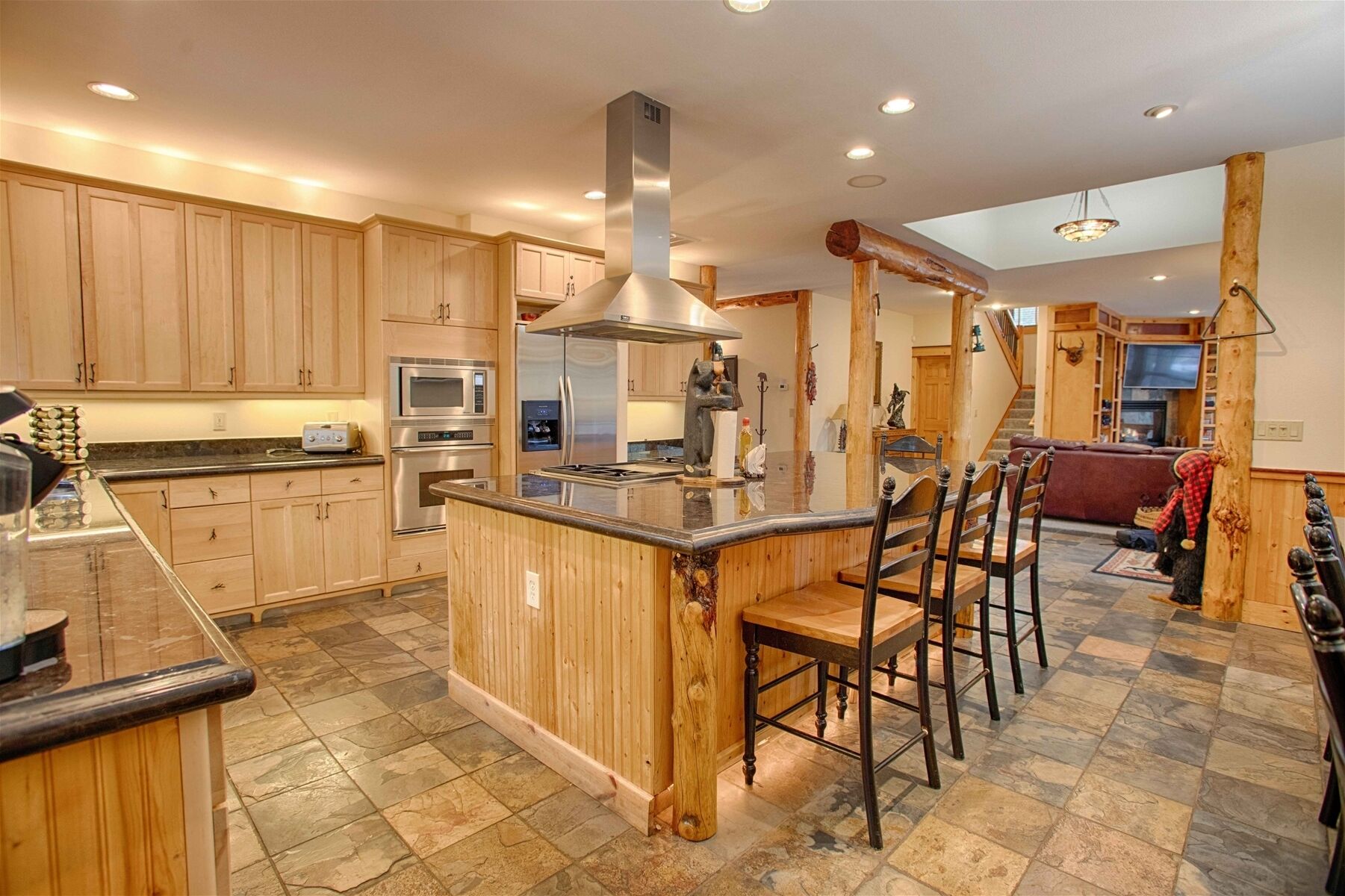 A spacious kitchen with wooden cabinets, a central island with bar stools, a microwave, oven, and a stainless steel range hood.