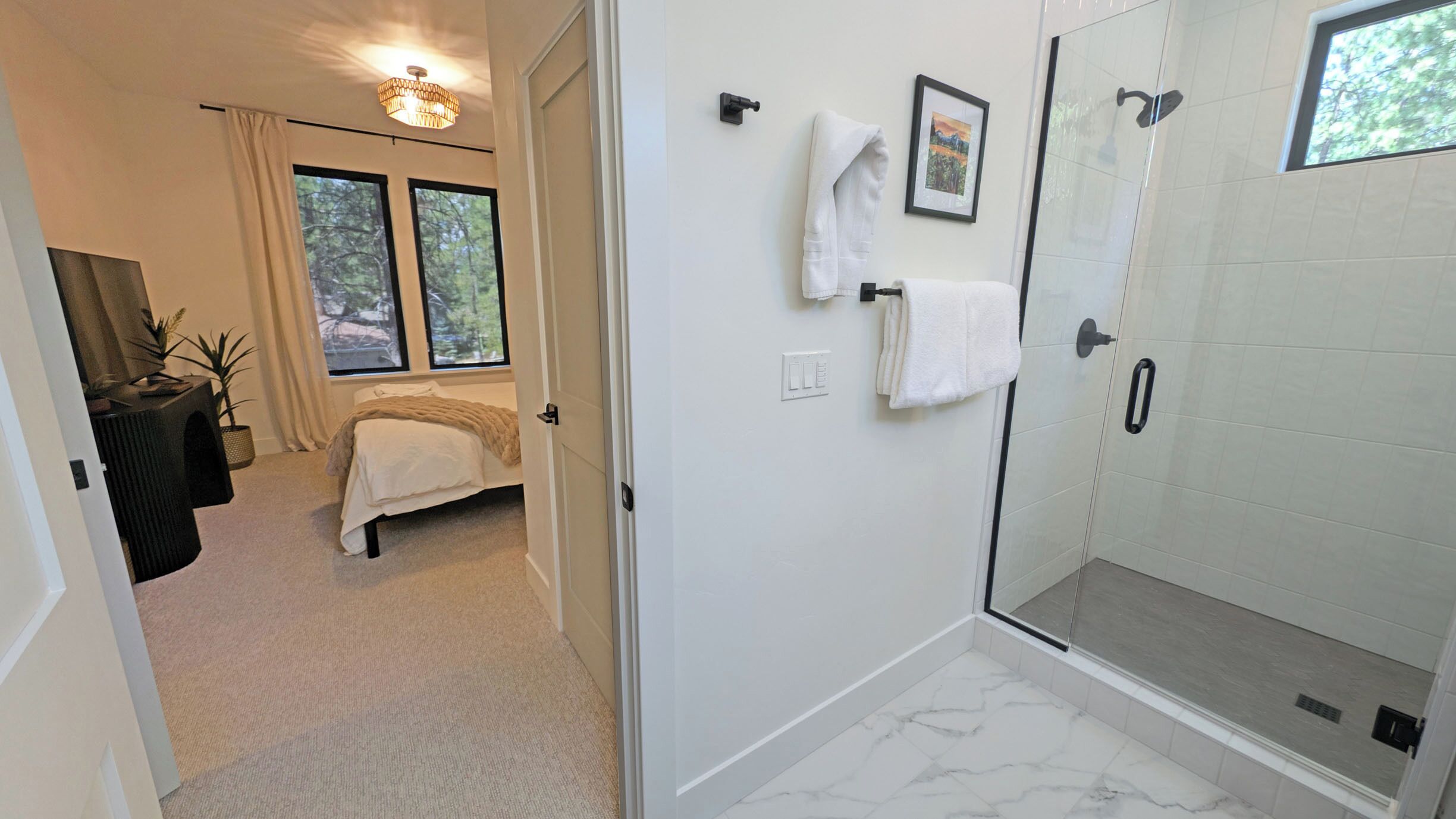 Un dormitorio con cama, mesita de noche, ventana y puerta que da a un baño con ducha.