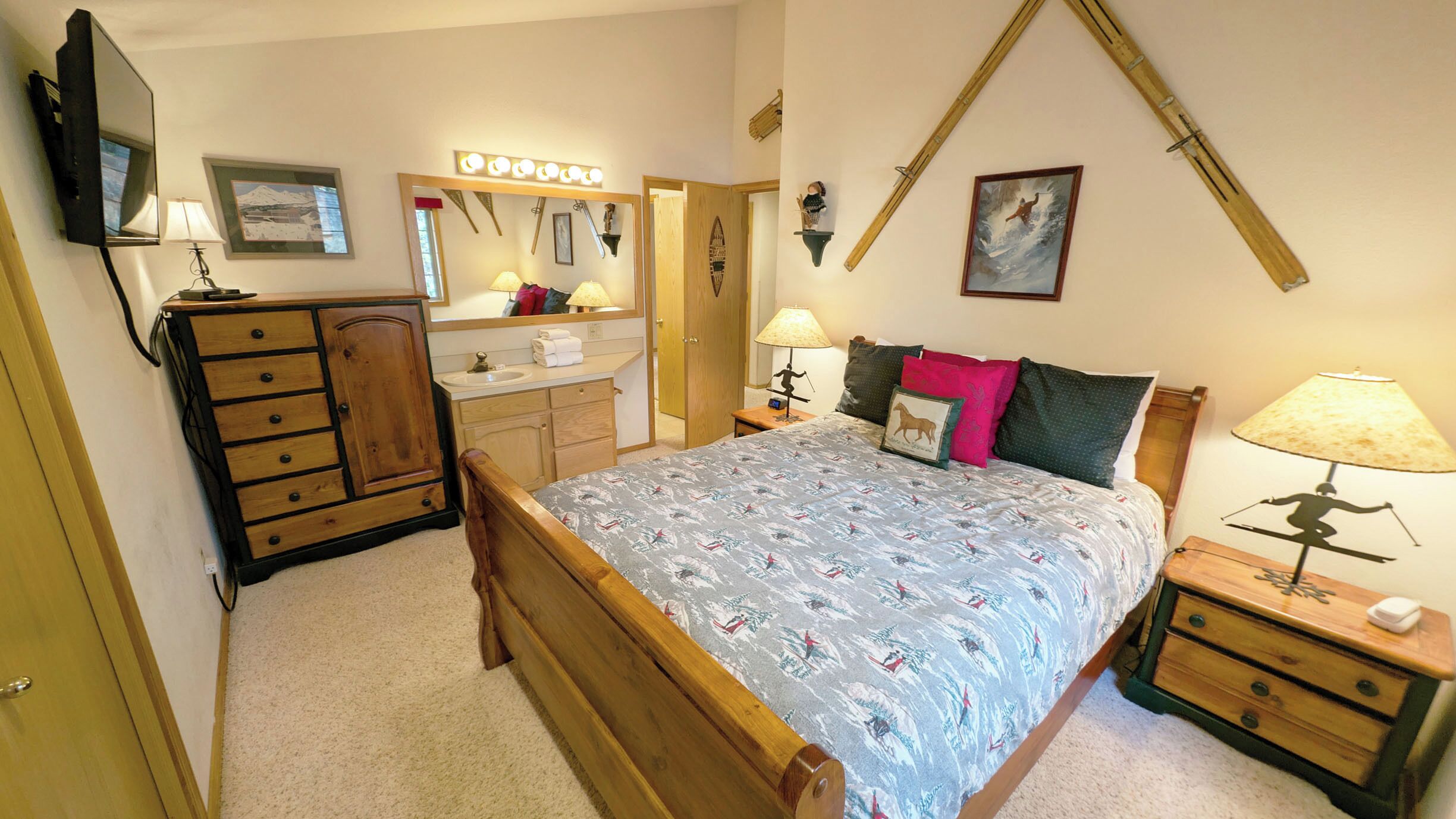 A bedroom with a wooden bed, a nightstand with a lamp, a dresser, a mirror, and a television.