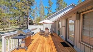A wooden deck with a grill and outdoor furniture, surrounded by trees and a house. - Snowshoe Inn-pyramid Mtn 7 (Bend)