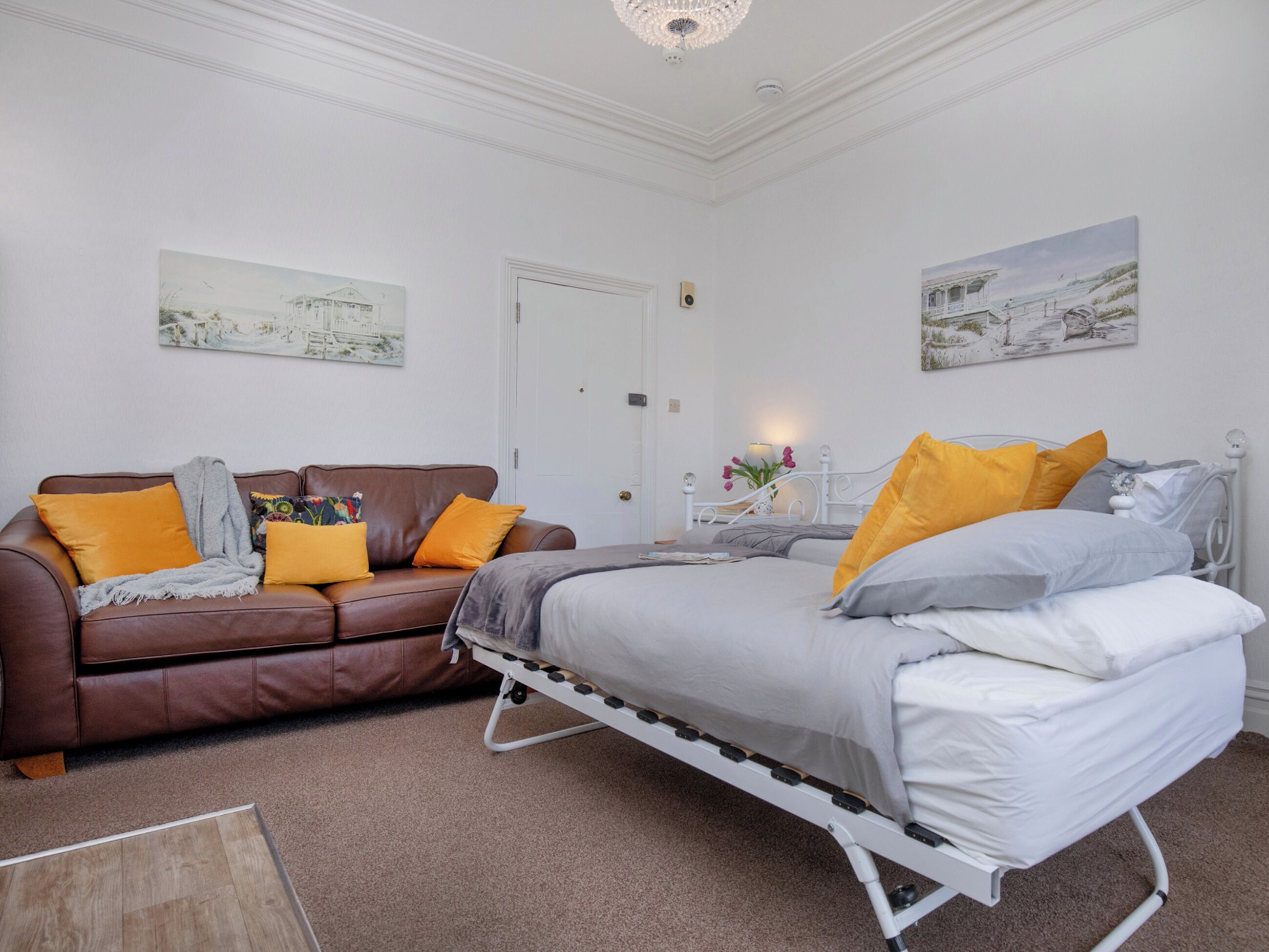 A bedroom with a bed, a brown leather sofa, and two wall-mounted paintings.