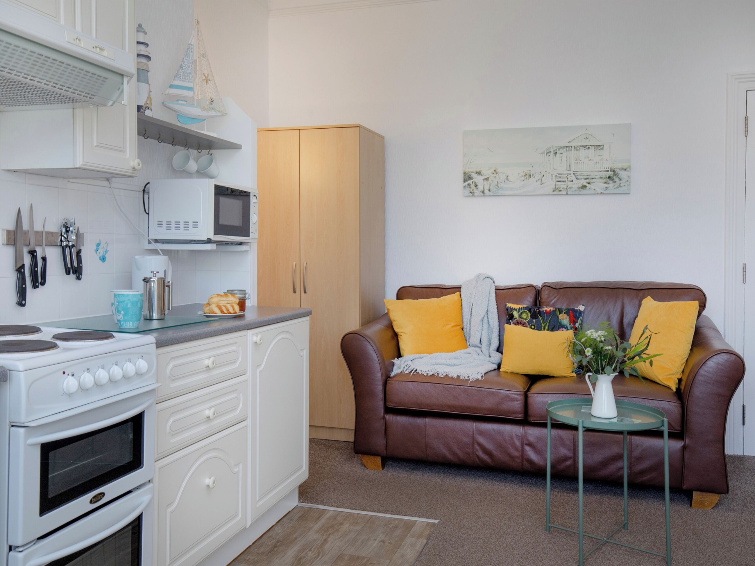 A compact living space with a kitchenette, a brown leather sofa, and a small round table with a vase.