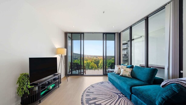 Un salón moderno con televisor de pantalla plana, sofá, alfombra estampada y balcón con vistas.