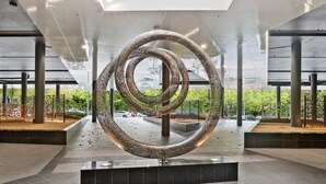 Una escultura moderna en un vestíbulo amplio con techo alto y ventanas grandes.