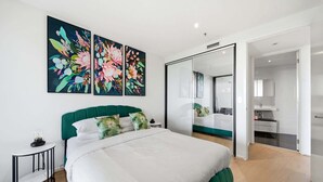 Un dormitorio moderno con un cabecero tapizado en verde, una cama grande con ropa de cama blanca, una mesita de noche y un espejo.