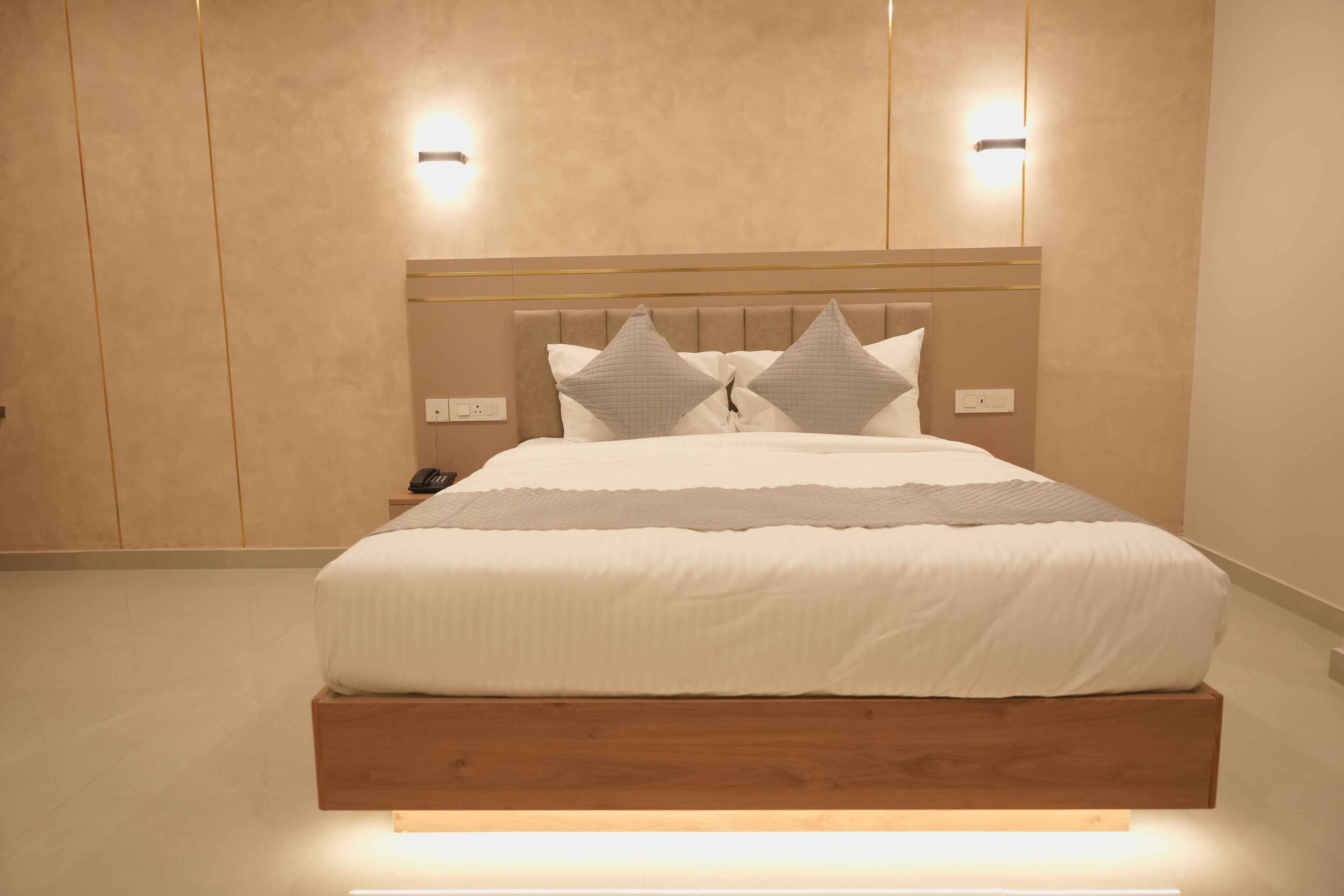 Un dormitorio moderno con estructura de cama de madera, cabecera con iluminación integrada y dos lámparas fijadas a la pared.