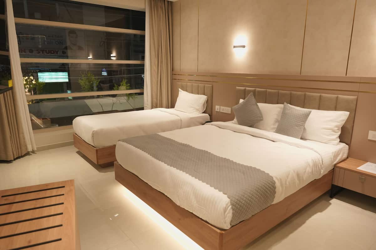 Habitación de hotel con dos camas, una mesita de noche, una mesita auxiliar de madera y un ventanal con cortinas.
