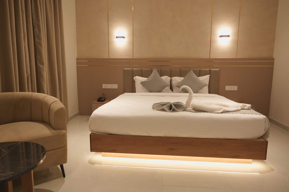 Una habitación de hotel moderna con una cama grande, un sofá, una mesita de noche y una lámpara de pared.