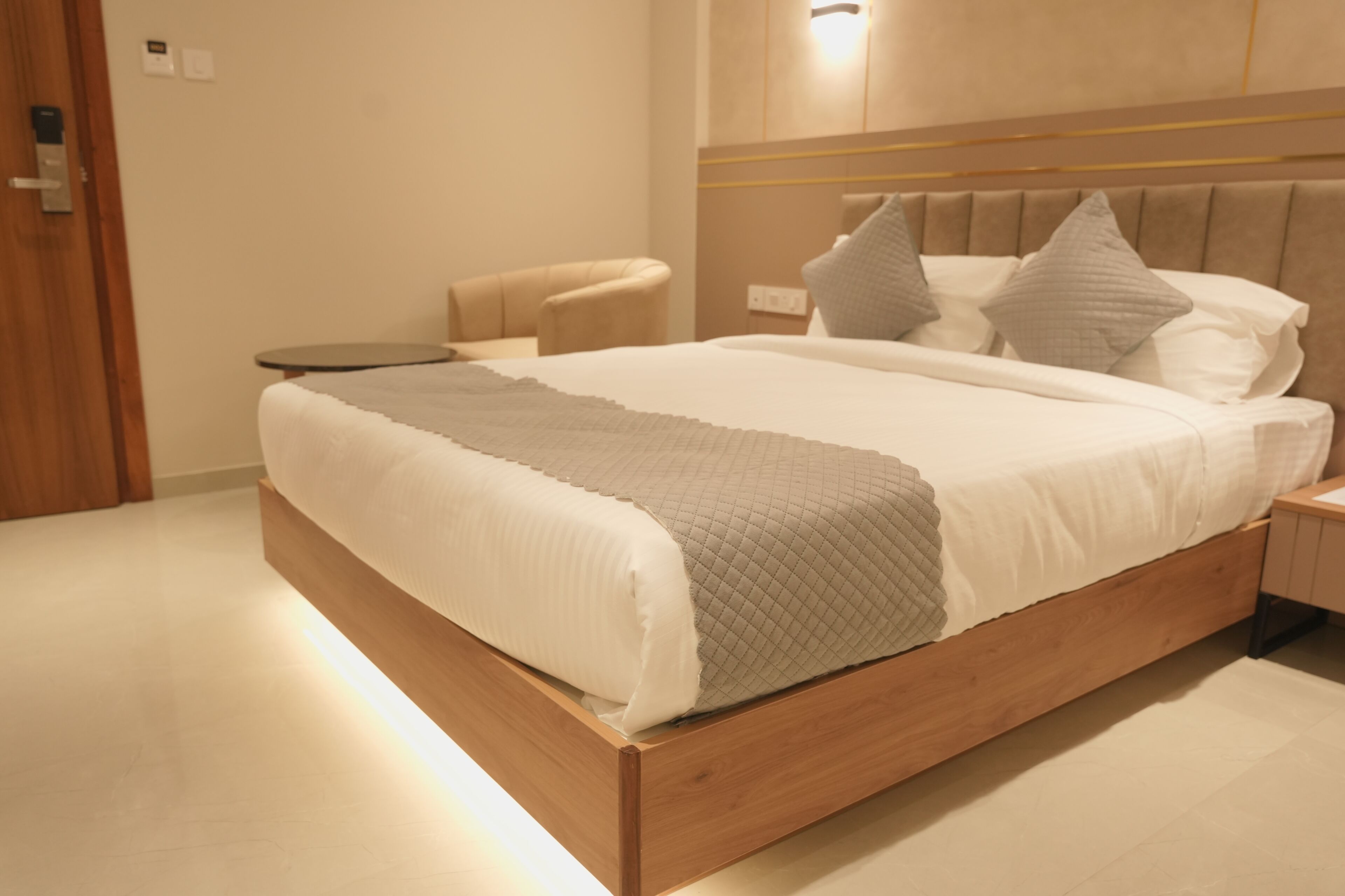A modern bedroom with a wooden bed, a bedside table, a chair, and a wall-mounted light fixture.