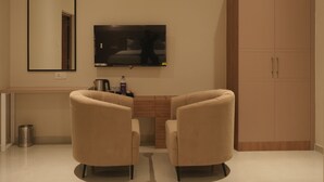 A modern hotel room with a flat-screen TV, two armchairs, a wooden cabinet, and a mirror on the wall.