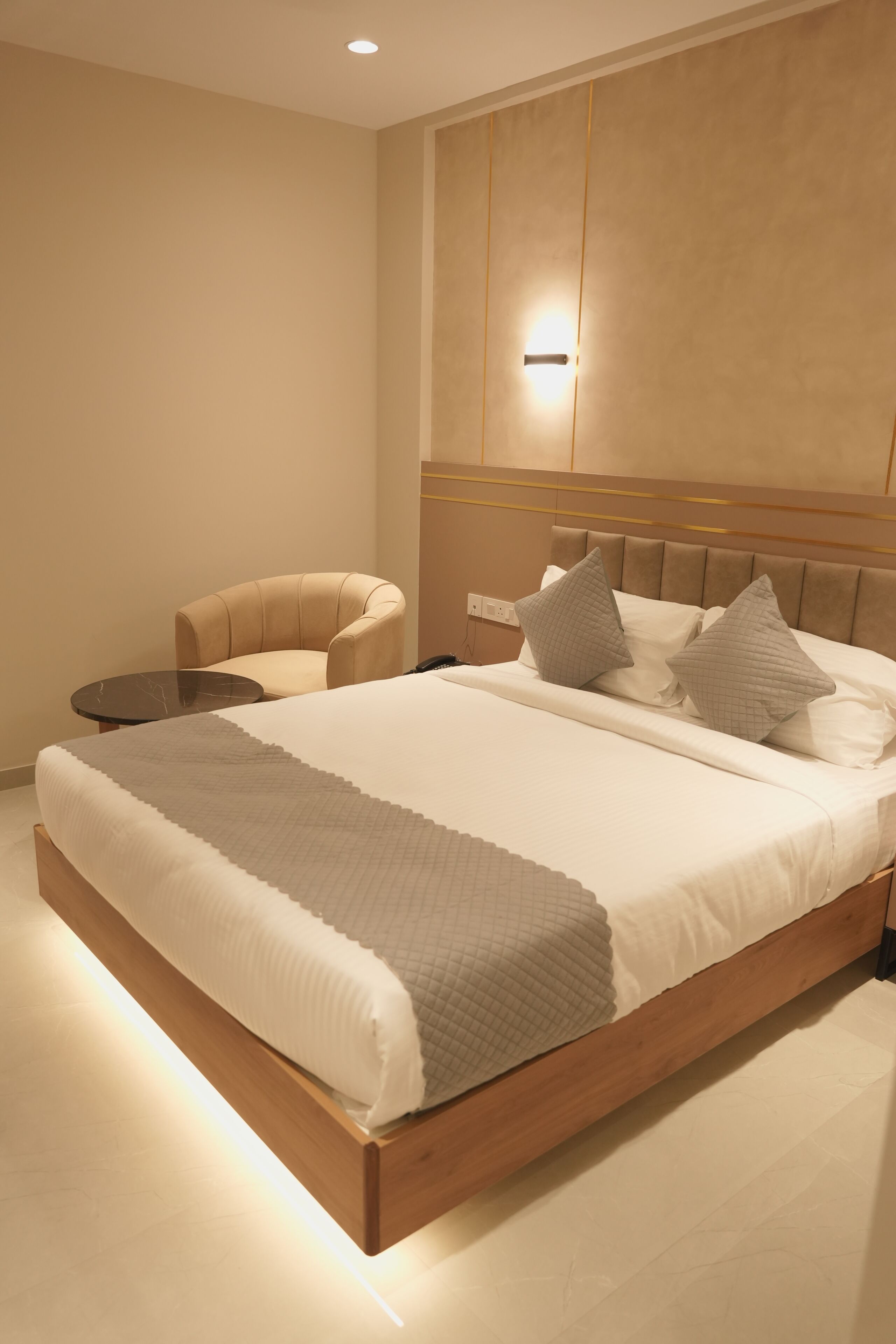 Un dormitorio moderno con una cama grande, una silla, una mesita de noche y una lámpara de pared.