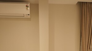 A room with two beige armchairs, a small round table, a wall-mounted air conditioner, and a window with beige curtains.