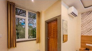 A room with a wooden door, a window with curtains, a marble-patterned floor, and a wall-mounted air conditioning unit. - Hotel Heaven Palace And Banquet (Jaipur)