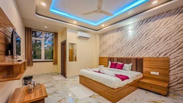 A bedroom with a bed, a ceiling fan, a TV, a window, and a marble floor. - Hotel Heaven Palace And Banquet (Jaipur)