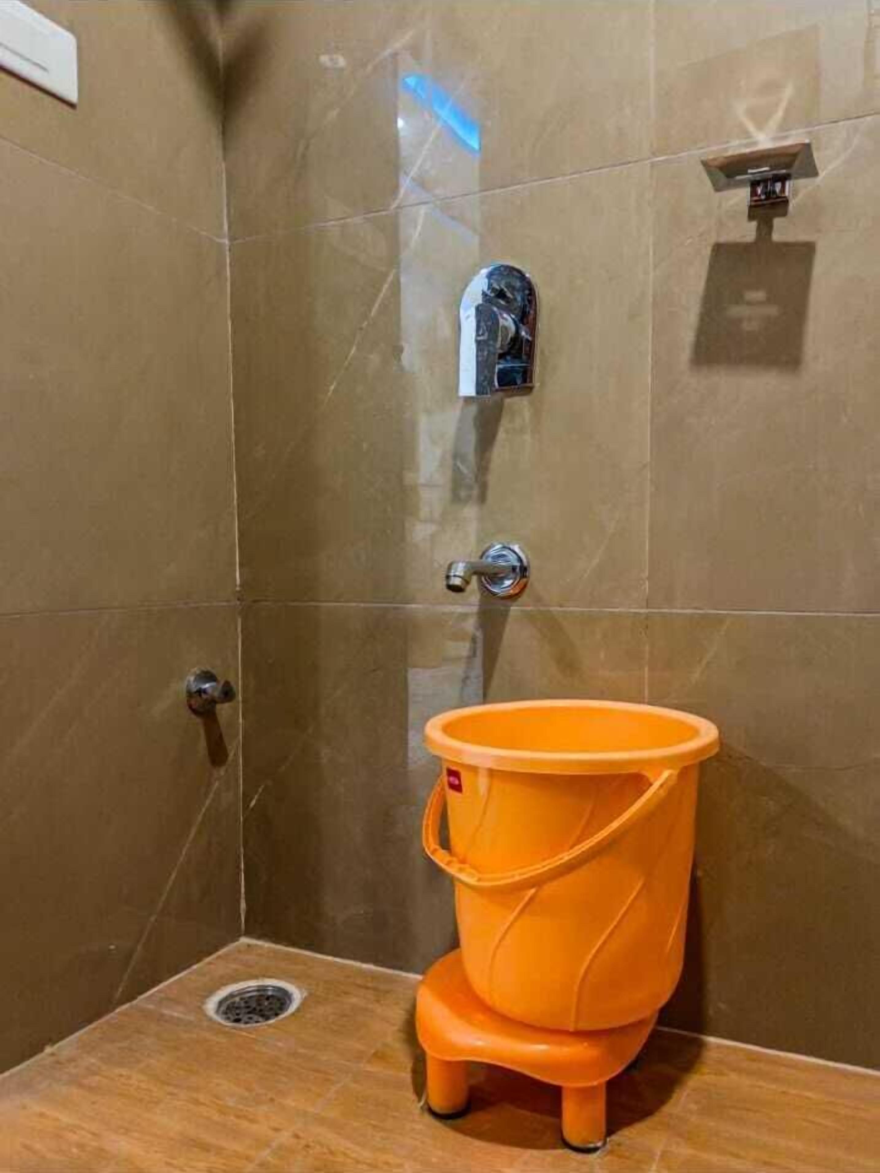 A bathroom with a shower, a toilet, and a small orange bucket.