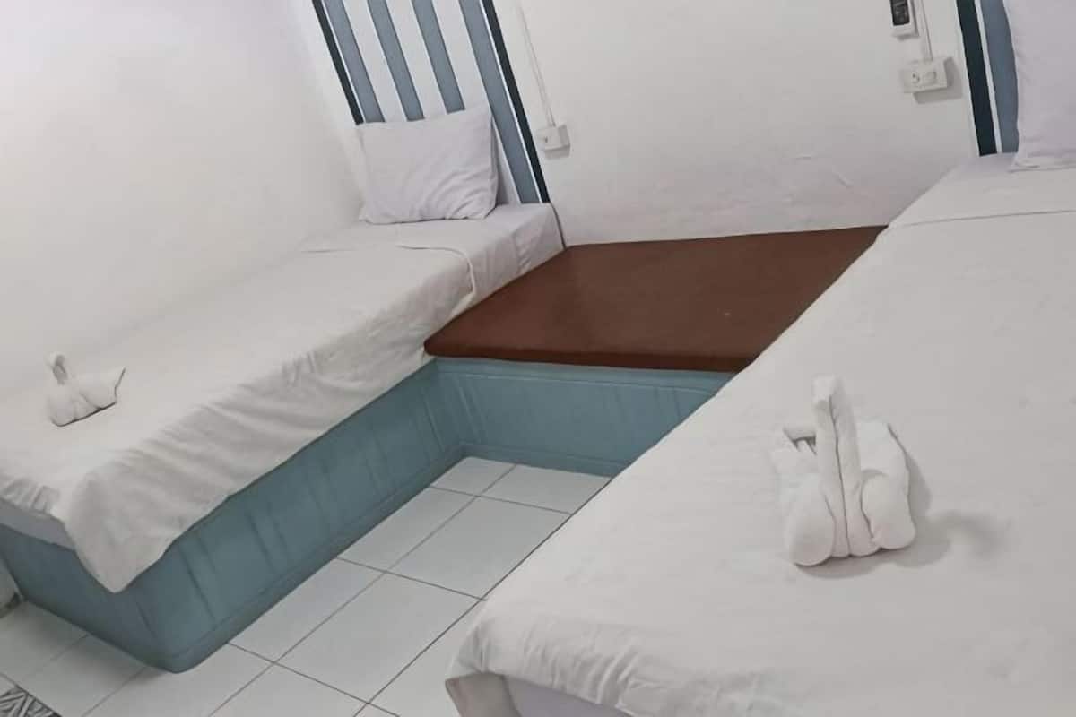 A room with two beds, each with white linens and pillows, a brown mattress in the center, and a tiled floor.