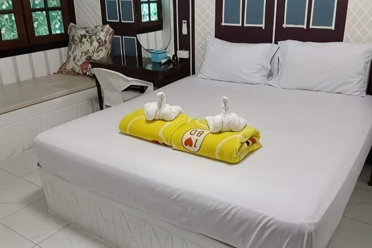 A neatly made bed with a yellow towel and white swan-shaped towels, a white headboard, a window with a view, and a small bedside table with a lamp.