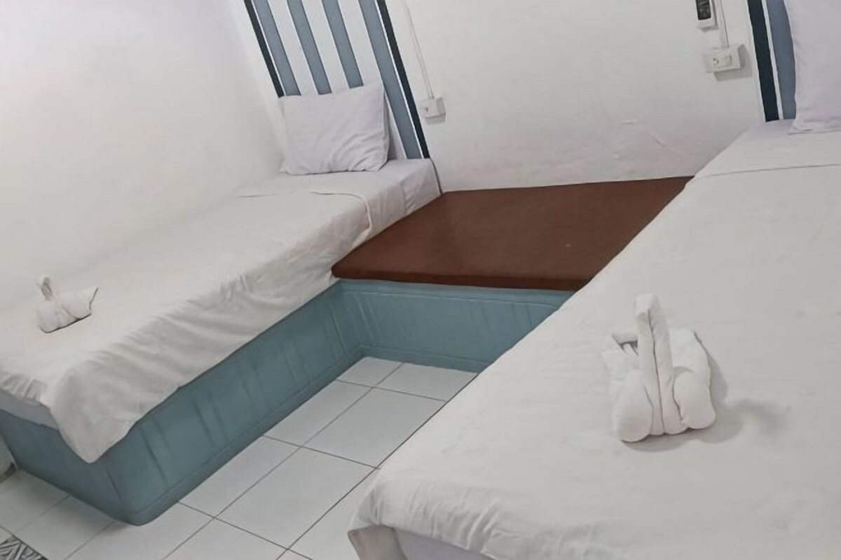 A room with two beds, each with white linens and pillows, a brown mattress in the center, and a tiled floor.