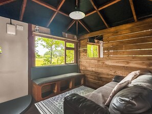 Ein gemütliches Blockhaus-Interieur mit einer Holzwand, einer Bank, einem Sofa und einem Fenster mit Blick auf Grünflächen.