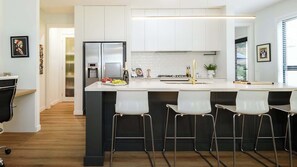 Una cocina moderna con muebles blancos, un refrigerador de acero inoxidable, una botella de vino y una zona de bar con taburetes blancos.