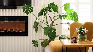 Una sala de estar con una planta grande, una chimenea, un televisor y una mesa con un florero.