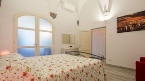 Un dormitorio con cama, espejo, puerta y un cuadro en la pared.