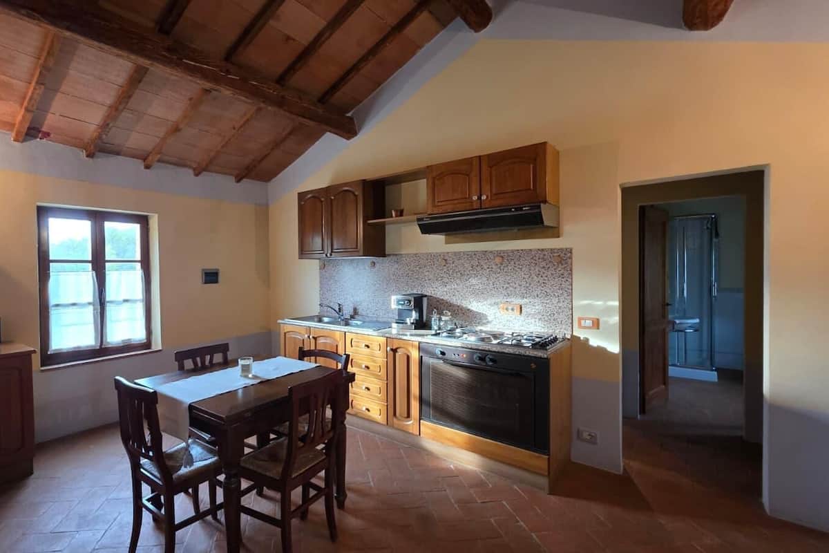 A kitchen with wooden cabinets, a dining table with chairs, a stove, and a window.