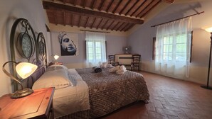 A bedroom with a bed, bedside lamp, artwork, chairs, and a desk. - La Tresa Country Living (Montepulciano)