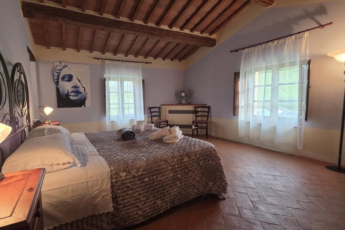 A bedroom with a bed, bedside lamp, artwork, chairs, and a desk.