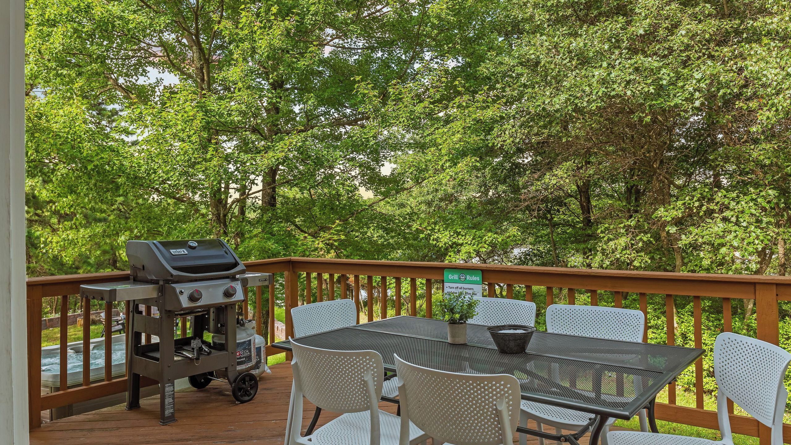 A covered outdoor patio with a grill, seating, and a view of trees.