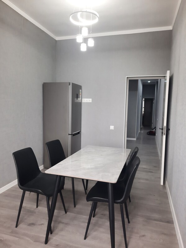 Un comedor con una mesa de mármol, sillas negras, un refrigerador gris y una lámpara en el techo.