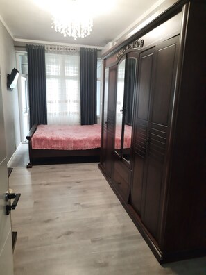 Un dormitorio con cama, armario, candelabro y ventana con cortinas.