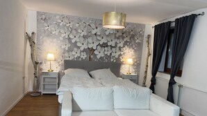 Quarto com cama, duas mesas de cabeceira, luminária na parede, luminária de chão e janela com cortinas.