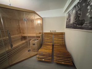 A sauna room with wooden benches, a glass enclosure, and a wall-mounted heater. - Vacation home in Braunlage (Braunlage)