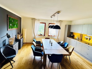 A dining area with a wooden table, blue chairs, a chandelier, and a view of the outdoors through windows. - Vacation home in Braunlage (Braunlage)