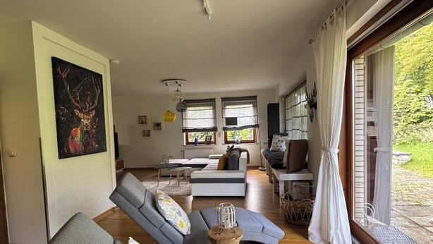 Uma sala de estar moderna com sofás cinza, uma mesa de centro de madeira e uma janela grande com cortinas.