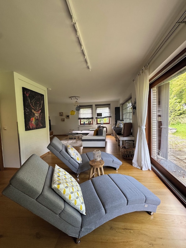 A modern living room with grey sofas, a wooden coffee table, and a large window with curtains. - Vacation home in Braunlage (Braunlage)