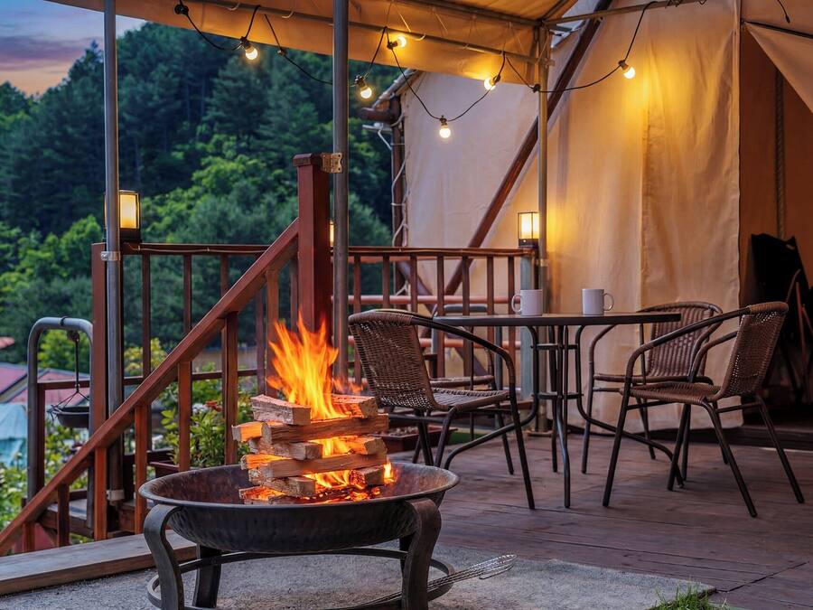 A fire pit with logs, wicker chairs, a table, and a view of a forested area.
