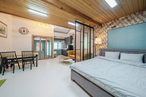 A bedroom with a large bed, a dining area with chairs, a kitchen, and a living area with a sofa.