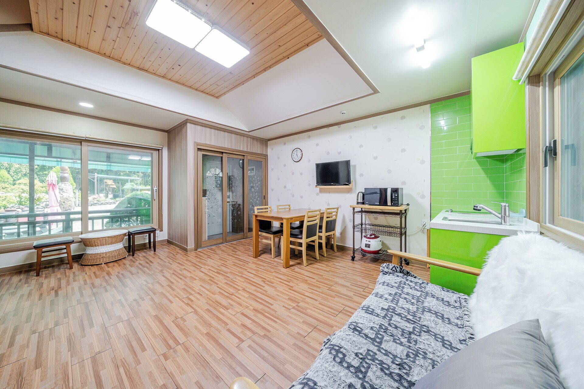 Una sala de estar moderna con comedor, cocina con detalles en verde y un amplio ventanal con vistas a un jardín.