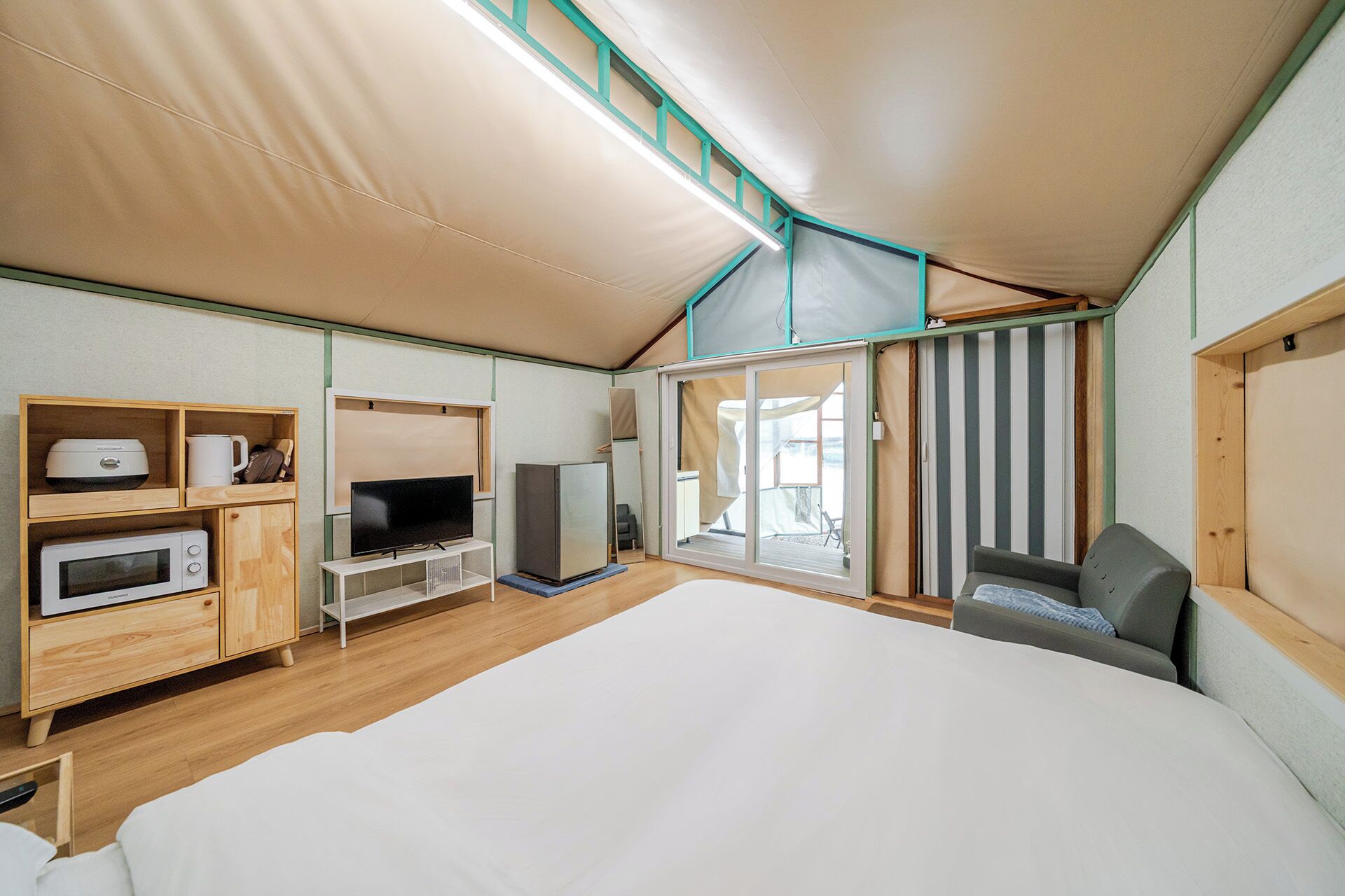 A tent-style room with a bed, a television, a microwave, and a refrigerator.