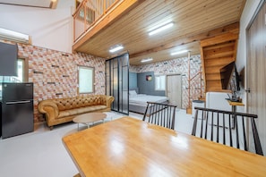 A compact living space with a kitchenette, a sofa, a dining table, and a bedroom with a bed and a window.