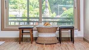 A room with a large window, two wooden stools, a wicker table, and a view of greenery and a statue outside. - Pocheon Terrace 527 Campground (Pocheon)