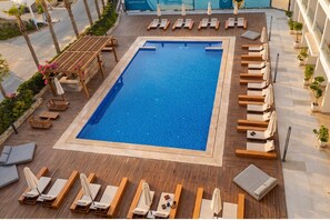 A pool area with lounge chairs, a wooden deck, and a view of the street. - Casa White (El Alamein)