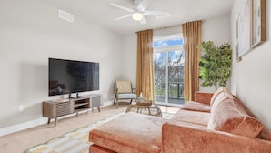 A living room with a flat-screen TV, a sofa, a chair, a small table, and a plant.