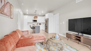 A living room with a sofa, a television, and a kitchen in the background.